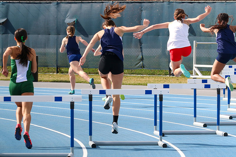 Rear view of girls running a 400 meter hurdle race